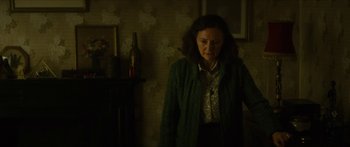 Movie still from “Calm with Horses” (2019), directed by Nick Rowland – A woman standing in a room with a bottle of wine; Medium shot, Over the shoulder angle
