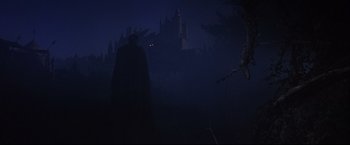 Movie still from “Camelot” (1967), directed by Joshua Logan – A man in a black cape standing in front of a castle; Extreme Wide shot, Low angle