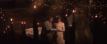 Movie still from “Camelot” (1967), directed by Joshua Logan – A man and a woman standing in front of lit candles; Wide shot, High angle