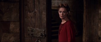 Movie still from “Camelot” (1967), directed by Joshua Logan – A woman in a red dress standing in front of a wooden door; Medium shot, Over the shoulder angle