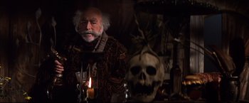 Movie still from “Camelot” (1967), directed by Joshua Logan – An old man with a beard is standing in front of a skull; Close Up shot, Low angle