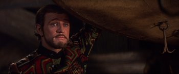 Movie still from “Camelot” (1967), directed by Joshua Logan – A man with a beard is holding on to a large object; Medium shot, Over the shoulder angle