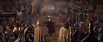 Movie still from “Camelot” (1967), directed by Joshua Logan – A group of people in costumes in a room with statues; Wide shot, High angle