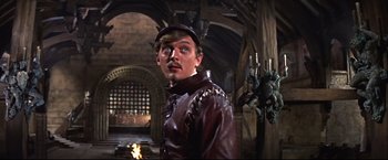 Movie still from “Camelot” (1967), directed by Joshua Logan – A man wearing a leather jacket and hat in a room; Medium shot, Low angle