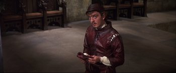 Movie still from “Camelot” (1967), directed by Joshua Logan – A man in a leather jacket holding a pair of shoes; Medium shot, High angle