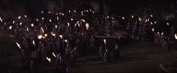 Movie still from “Camelot” (1967), directed by Joshua Logan – A group of people are holding torches in the dark; Extreme Wide shot, High angle