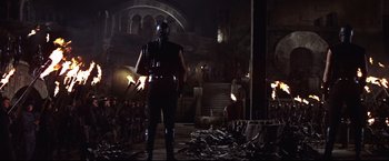 Movie still from “Camelot” (1967), directed by Joshua Logan – A man in a black leather outfit stands in front of a group of people; Wide shot, Low angle