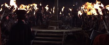 Movie still from “Camelot” (1967), directed by Joshua Logan – A group of people on a stage in front of fire; Wide shot, High angle