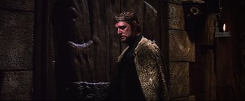 Movie still from “Camelot” (1967), directed by Joshua Logan – A man wearing a crown standing in front of a wooden wall; Medium shot, Low angle
