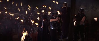 Movie still from “Camelot” (1967), directed by Joshua Logan – A group of people dressed in costumes and holding torches in front of a crowd of onlookers; Wide shot, High angle