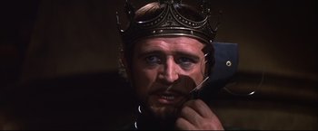 Movie still from “Camelot” (1967), directed by Joshua Logan – A person wearing a crown holding a pair of scissors; Close Up shot, Over the shoulder angle