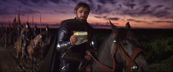 Movie still from “Camelot” (1967), directed by Joshua Logan – A man wearing a suit of armor and holding a letter; Medium shot, Over the shoulder angle