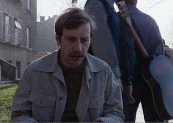 Movie still from “Camera Buff” (1979), directed by Krzysztof Kieslowski – A man sitting on a bench with a guitar in front of him; Medium shot, Over the shoulder angle