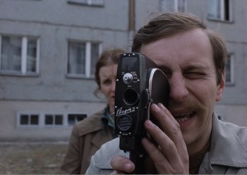 Movie still from “Camera Buff” (1979), directed by Krzysztof Kieslowski – A man holding an old camera up to his face; Close Up shot, Over the shoulder angle