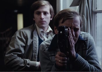 Movie still from “Camera Buff” (1979), directed by Krzysztof Kieslowski – A man taking a picture of another man with a camera; Close Up shot, Over the shoulder angle