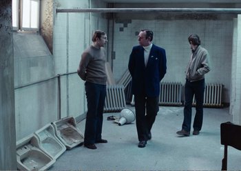 Movie still from “Camera Buff” (1979), directed by Krzysztof Kieslowski – A group of men standing around in a room; Wide shot, High angle