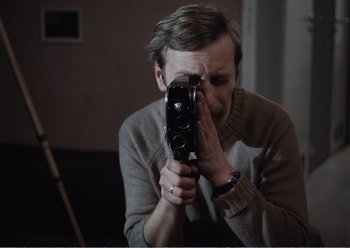 Movie still from “Camera Buff” (1979), directed by Krzysztof Kieslowski – A man holding an old camera up to his face; Close Up shot, Over the shoulder angle