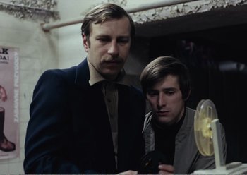 Movie still from “Camera Buff” (1979), directed by Krzysztof Kieslowski – Two men looking at something on a phone; Medium shot, Low angle