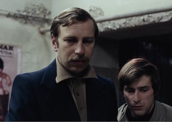 Movie still from “Camera Buff” (1979), directed by Krzysztof Kieslowski – Two men standing next to each other in front of a wall; Close Up shot, Low angle