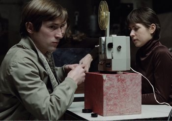 Movie still from “Camera Buff” (1979), directed by Krzysztof Kieslowski – A man and a woman looking at an old movie projector; Medium shot, High angle