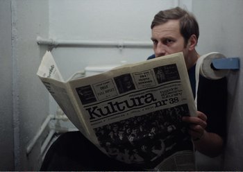 Movie still from “Camera Buff” (1979), directed by Krzysztof Kieslowski – A man sitting down reading a newspaper; Medium shot, Low angle