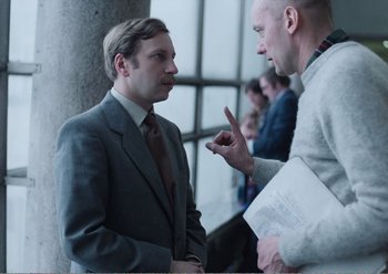 Movie still from “Camera Buff” (1979), directed by Krzysztof Kieslowski – Two men in business suits talking to each other; Medium shot, Over the shoulder angle