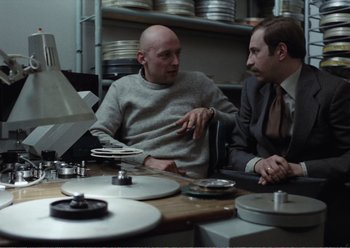 Movie still from “Camera Buff” (1979), directed by Krzysztof Kieslowski – Two men sitting at a table talking to each other; Medium shot, Low angle