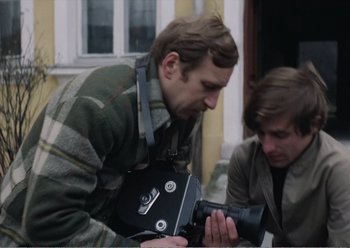 Movie still from “Camera Buff” (1979), directed by Krzysztof Kieslowski – Two men are looking at a film camera; Close Up shot, Low angle
