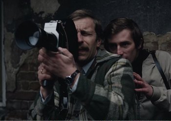 Movie still from “Camera Buff” (1979), directed by Krzysztof Kieslowski – A man holding an old fashioned camera next to another man; Close Up shot, High angle