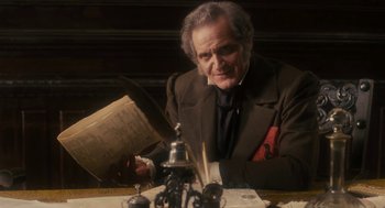 An older man sitting at a table reading a paper