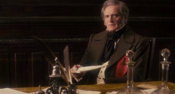 An older man sitting at a table with a quill pen