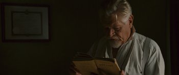 An older man reading a book in a dark room
