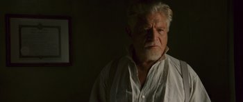 An older man in a white shirt is looking at the camera