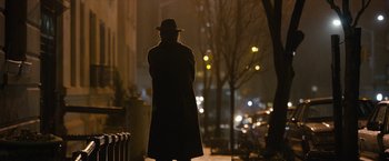 Movie still from “Can You Ever Forgive Me?” (2018), directed by Marielle Heller – A man in a long coat and a hat standing on a sidewalk; Wide shot, Over the shoulder angle