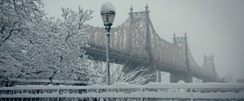 A street light covered in snow in front of a bridge