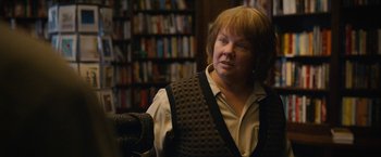 Movie still from “Can You Ever Forgive Me?” (2018), directed by Marielle Heller – A woman in a library wearing a vest; Close Up shot, Over the shoulder angle