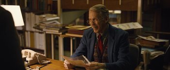 Movie still from “Can You Ever Forgive Me?” (2018), directed by Marielle Heller – An older man sitting at a table holding a piece of paper; Medium shot, Over the shoulder angle