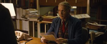 Movie still from “Can You Ever Forgive Me?” (2018), directed by Marielle Heller – An older man sitting at a table holding papers; Medium shot, Over the shoulder angle