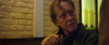 Movie still from “Can You Ever Forgive Me?” (2018), directed by Marielle Heller – An older man holding a fork in his right hand; Close Up shot, Over the shoulder angle