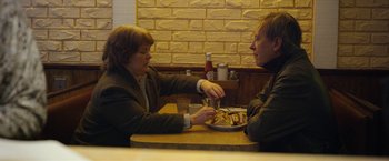 Movie still from “Can You Ever Forgive Me?” (2018), directed by Marielle Heller – A man and a woman sitting at a table with a plate of food in front of them; Medium shot, Over the shoulder angle