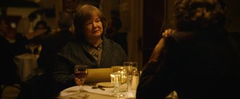 Movie still from “Can You Ever Forgive Me?” (2018), directed by Marielle Heller – An older woman sitting at a table with a glass of red wine; Medium shot, Over the shoulder angle