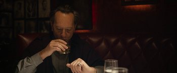 Movie still from “Can You Ever Forgive Me?” (2018), directed by Marielle Heller – A man sitting at a table with a drink in his hand; Close Up shot, Over the shoulder angle