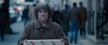 Movie still from “Can You Ever Forgive Me?” (2018), directed by Marielle Heller – A woman in a brown coat holding a box; Medium shot, Over the shoulder angle