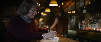 Movie still from “Can You Ever Forgive Me?” (2018), directed by Marielle Heller – An older woman writing on a piece of paper at a table; Medium shot, Over the shoulder angle