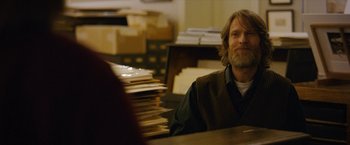Movie still from “Can You Ever Forgive Me?” (2018), directed by Marielle Heller – A man sitting at a table in front of stacks of papers; Medium shot, Over the shoulder angle