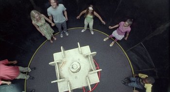 Movie still from “Candy” (2006), directed by Neil Armfield – A group of people standing around a fire pit; Wide shot, Overhead angle