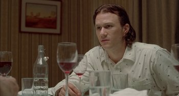 Movie still from “Candy” (2006), directed by Neil Armfield – A man sitting at a table with a glass of wine in front of him; Close Up shot, Over the shoulder angle
