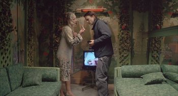 Movie still from “Candy” (2006), directed by Neil Armfield – A man and a woman standing next to each other in front of a television; Wide shot, High angle