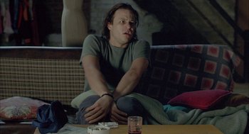 Movie still from “Candy” (2006), directed by Neil Armfield – A man sitting on a couch in a living room; Medium shot, Over the shoulder angle