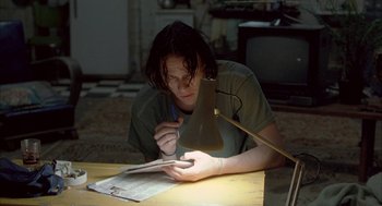 Movie still from “Candy” (2006), directed by Neil Armfield – A man sitting at a table writing on a piece of paper; Medium shot, Low angle